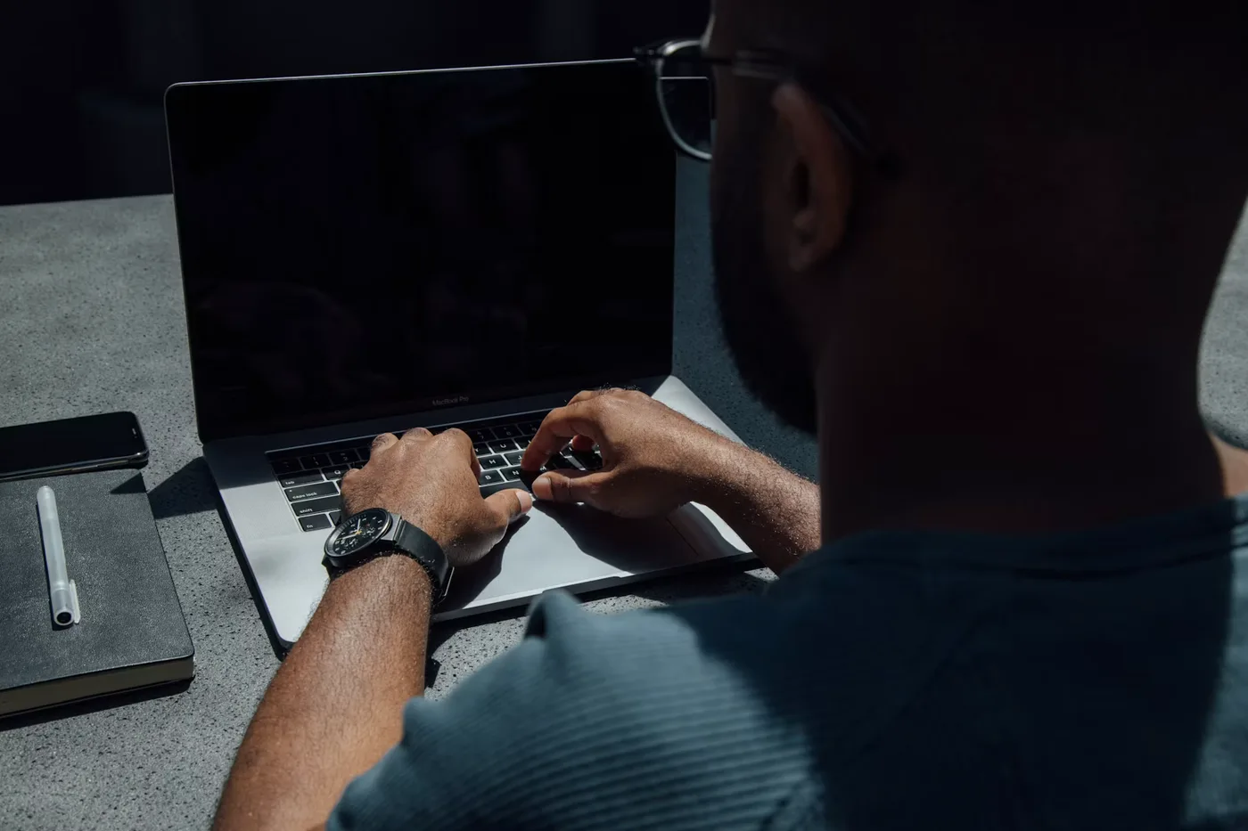 Hands working on a laptop beside a notebook